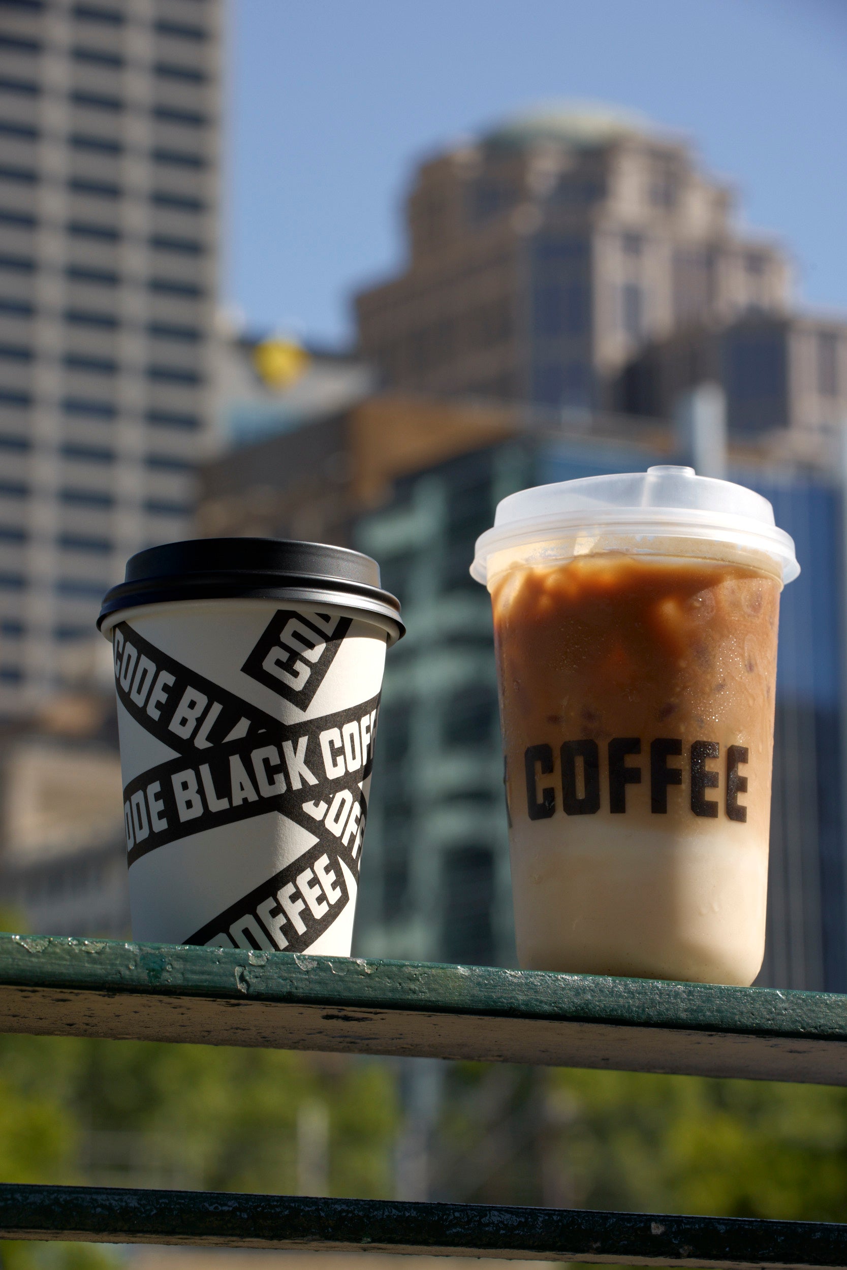 Two Code Black coffee cups on a ledge with a  Melbourne cityscape in the background